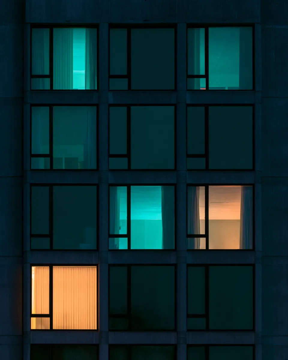 Rows of apartment windows at night, most dark, a few lit.