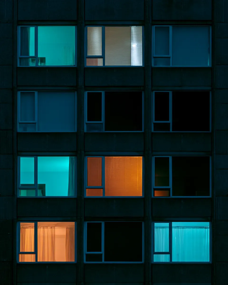 An apartment block at night, a few windows lit warm orange and cool teal.